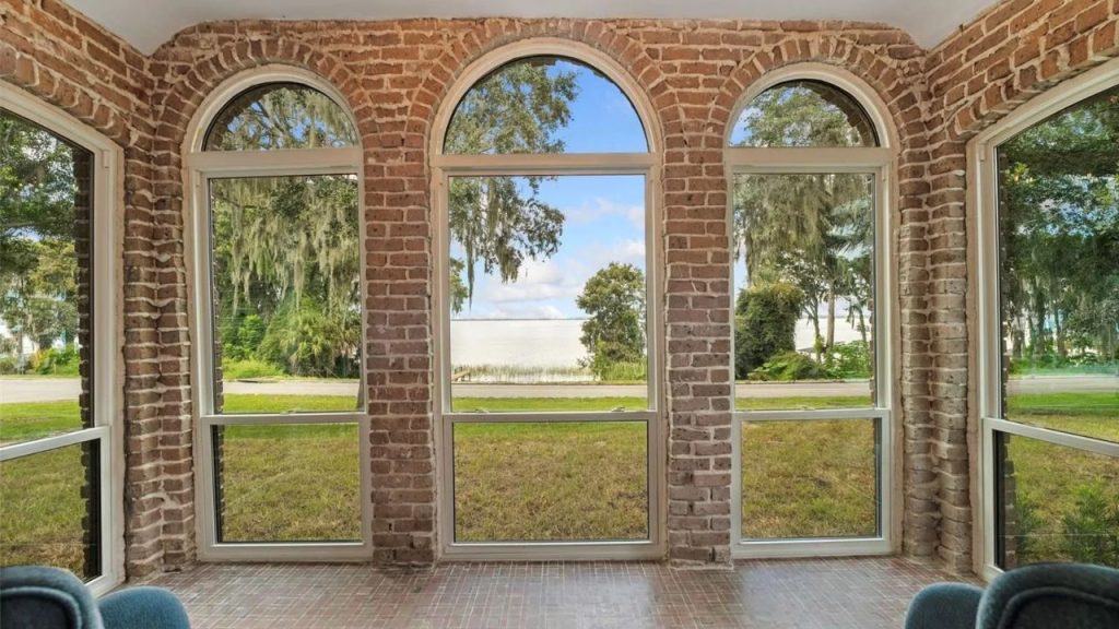 Brick sunroom with arched windows and tree-lined views.