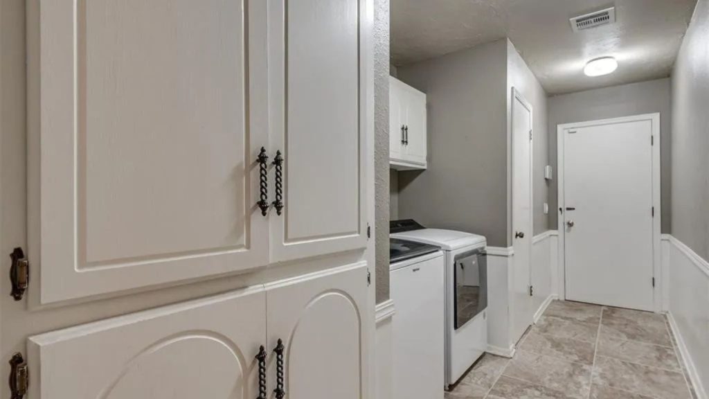 Laundry room with white cabinets, washer and dryer, and neutral wall tones.