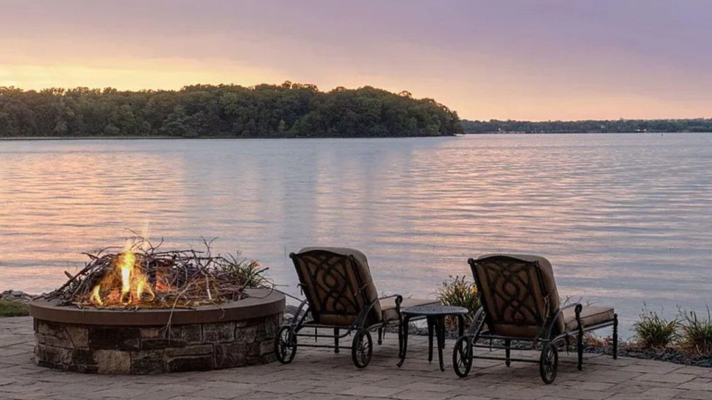 Lakeside fire pit with lounge chairs at sunset.