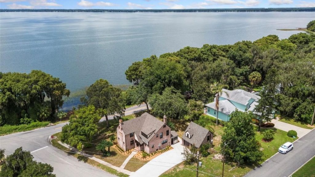 Brick colonial home near a lake with trees and a detached garage.