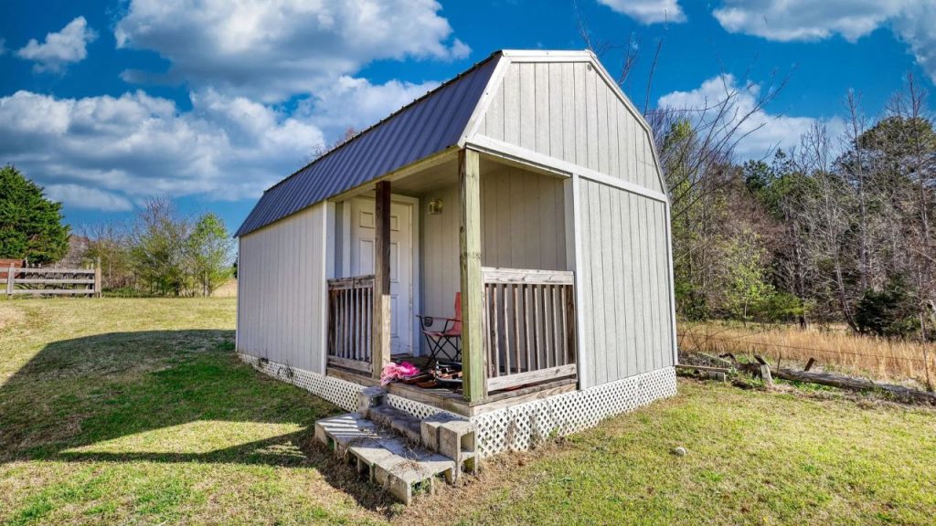 Small garden shed with porch, nestled in a grassy yard.