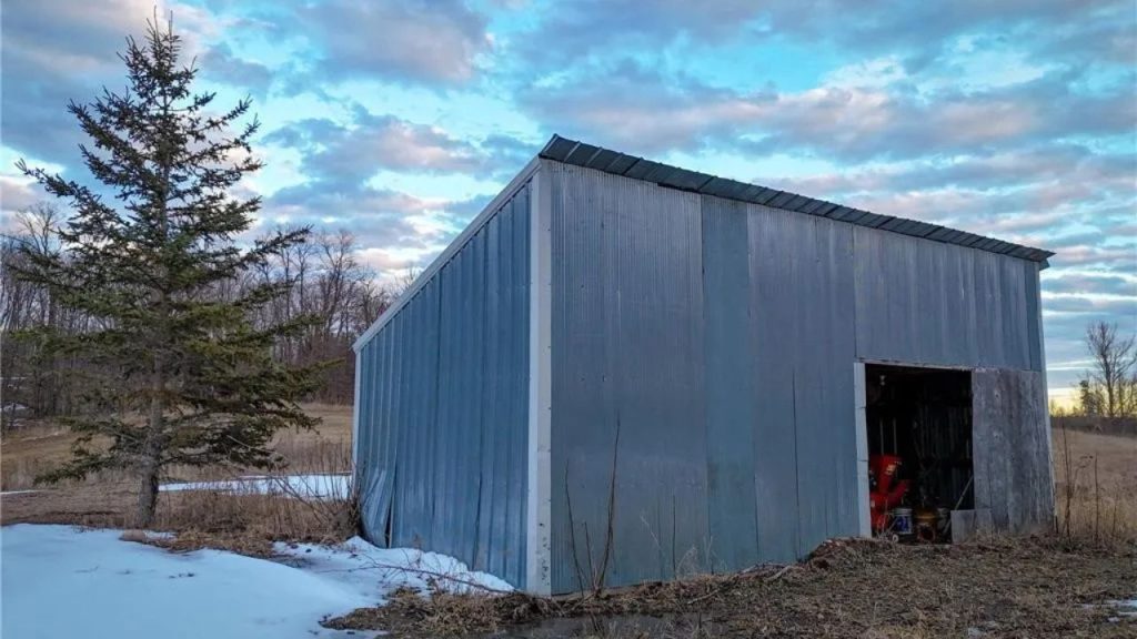 Corrugated metal shed in a snowy field with equipment inside.