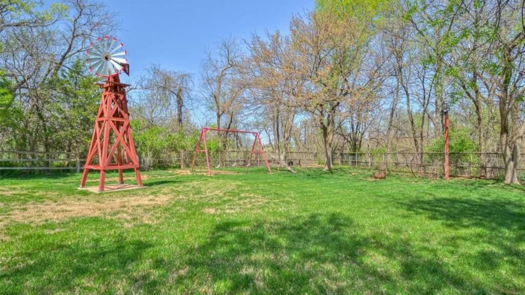 Grassy backyard with red windmill, swing set, and trees.