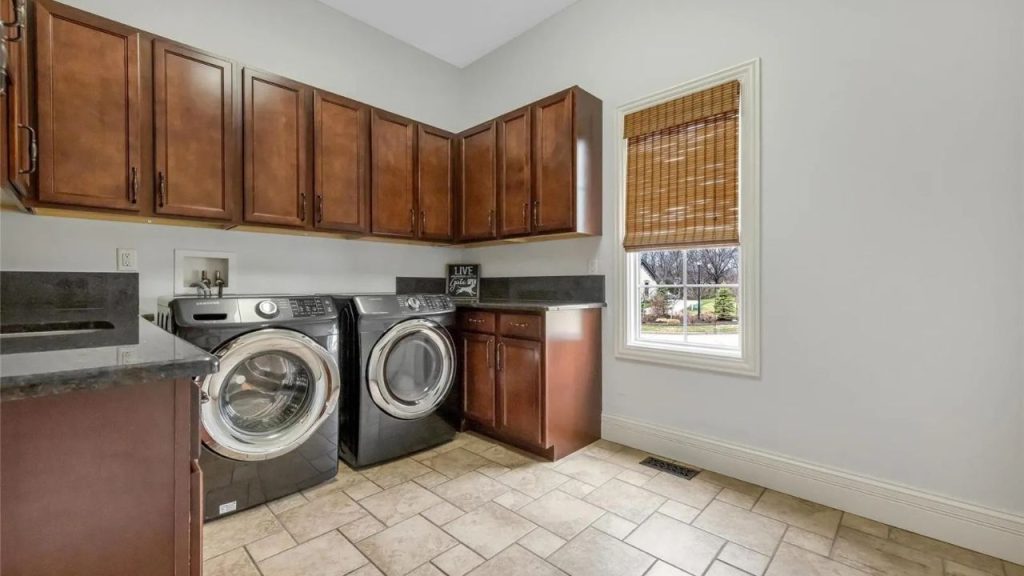 Laundry room with wooden cabinets, black washer and dryer, and a large window.