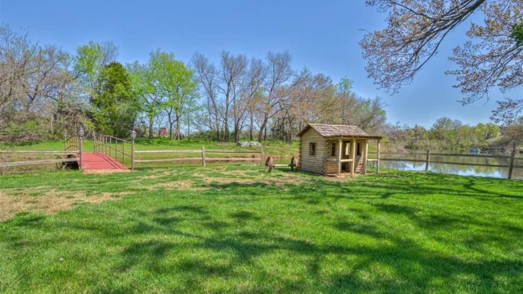Grassy backyard with playhouse, red bridge, and pond.