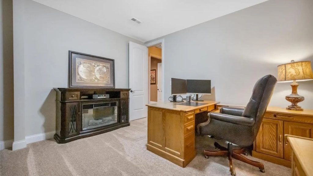 A warm and inviting home office with a wooden desk, dual monitors, a leather chair, and an electric fireplace.
