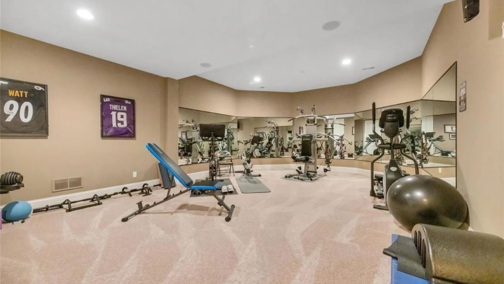 A spacious home gym with workout equipment, mirrors, and framed jerseys on the walls.