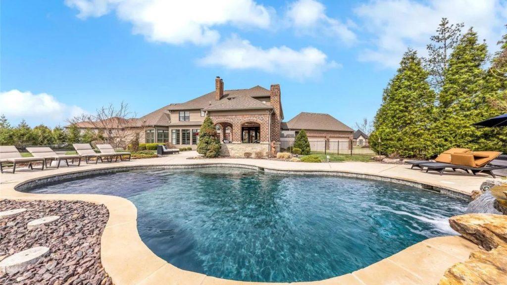 A luxurious backyard with a pool, lounge chairs, and a brick home in the background.
