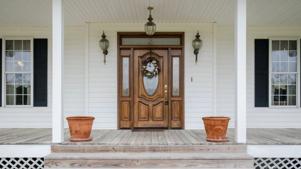 Wooden front door with glass panels on a white farmhouse porch.