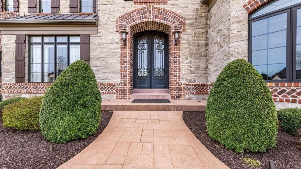 Elegant arched double door with brick and stone exterior, framed by manicured shrubs.
