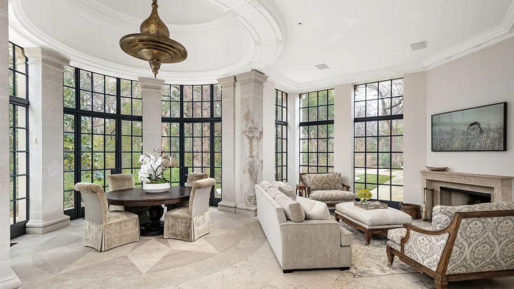 A bright living room with large windows, a chandelier, plush furniture, and a fireplace.