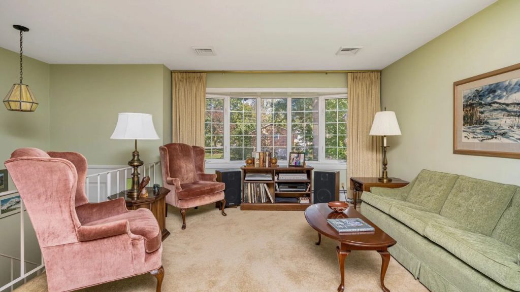 Vintage-style living room with large bay window, green sofa, and velvet chairs.