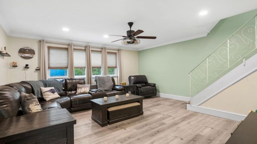 Living room with leather seating, soft green wall, and iron staircase railing.