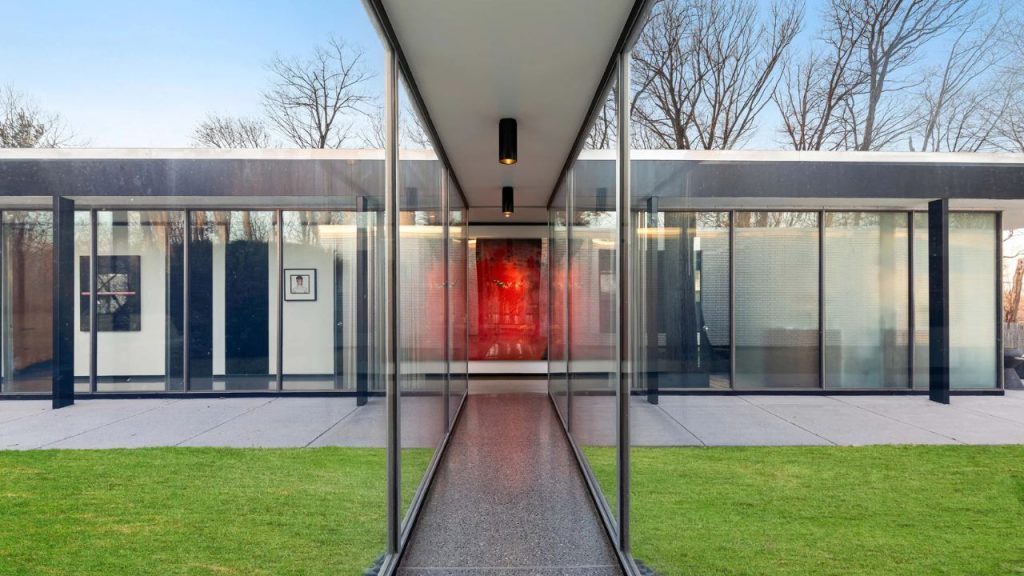 Modern glass hallway with red artwork at the end, connecting two sleek building sections.