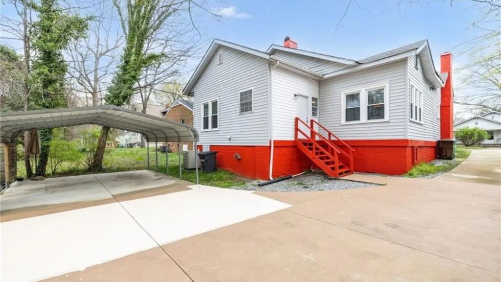 Back of a small house with red trim and a carport.