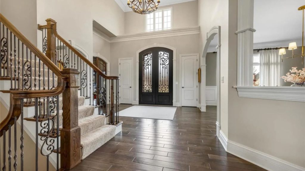 Spacious foyer with grand staircase, wrought iron double doors, and warm hardwood flooring.