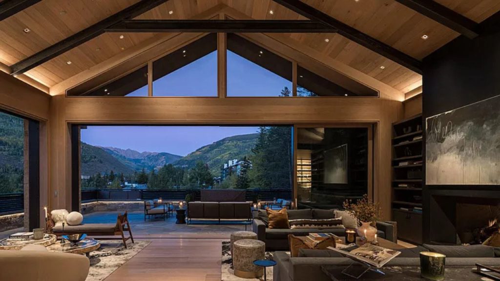 A cozy living area with high wooden beams, large windows, and mountain views at dusk.