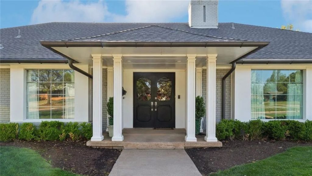 A stylish front entrance with white columns, black double doors, large windows, and a gray roof, surrounded by green hedges.