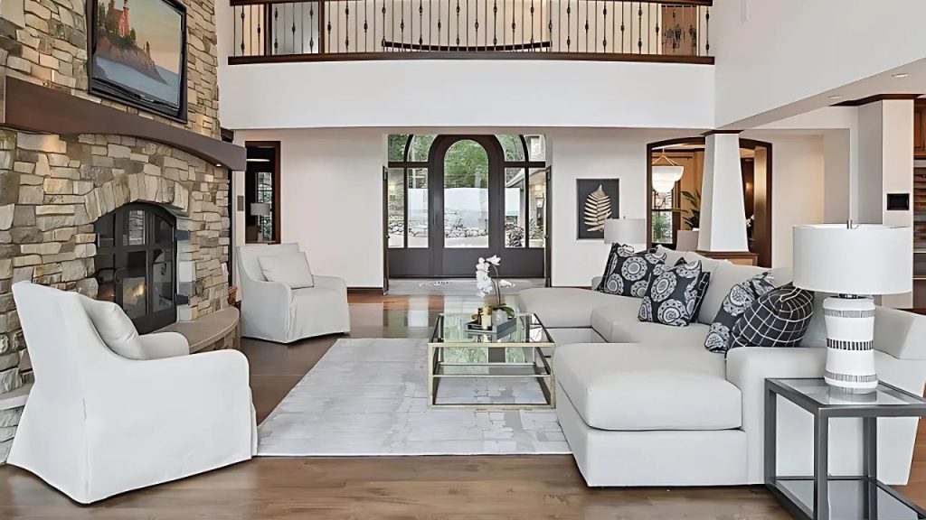 A bright living room with a stone fireplace, white sofas, and a view through an arched doorway.