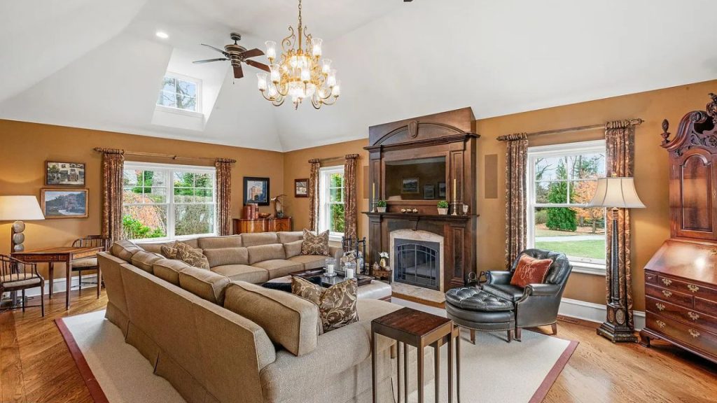A warm living room with a fireplace, chandelier, and large windows overlooking greenery.