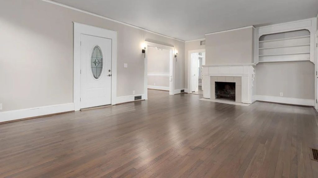 A spacious living room with hardwood floors, a white fireplace, built-in shelves, and an oval-windowed door.