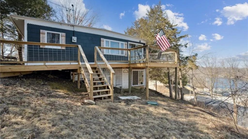 Elevated cabin with a wraparound deck overlooking a waterfront.