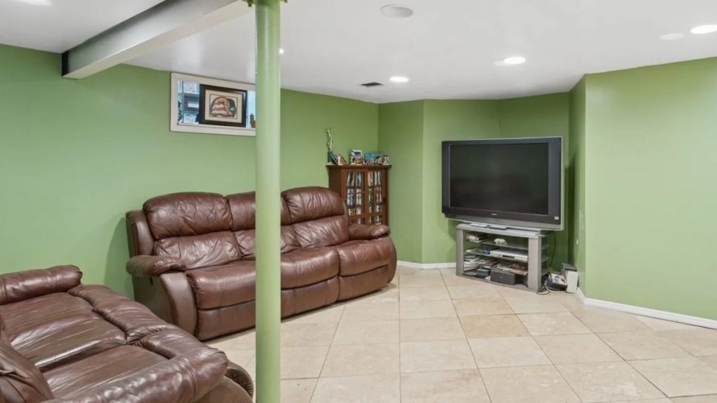 Green-walled basement with leather recliners and a large TV.
