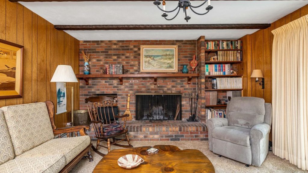 Wood-paneled room with brick fireplace, built-in bookshelves, and cozy vintage seating.