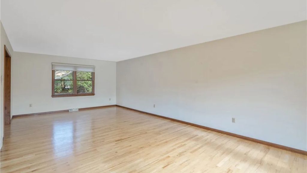Large living room with hardwood flooring, light walls, and a wide window.