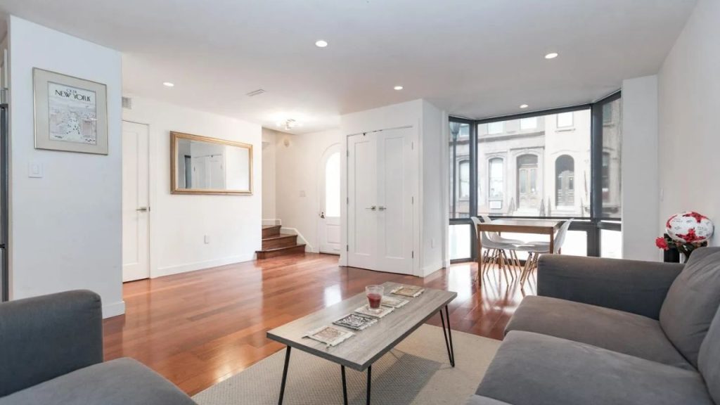 Bright open living room with hardwood floors, a bay window dining nook, and simple modern furniture.