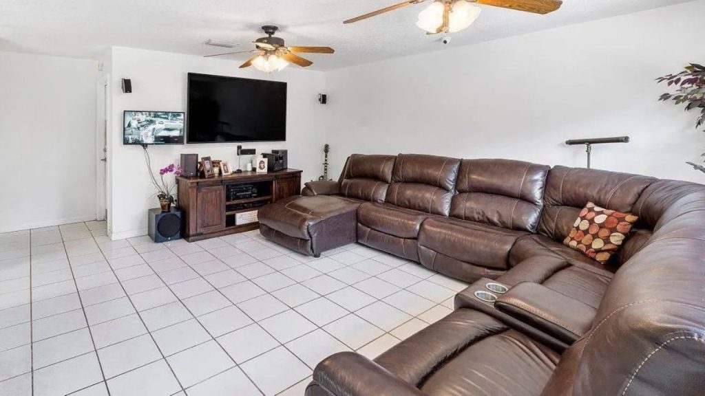 A cozy living room with a large leather sectional, TV setup, ceiling fans, and green plants.