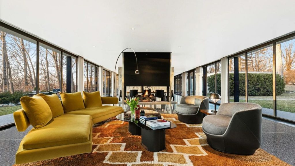 Glass-walled living room with bold furniture and a central fireplace.