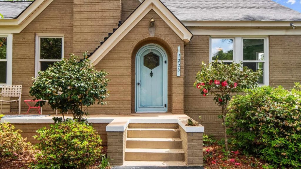 Brick house with a blue front door and small garden shrubs.