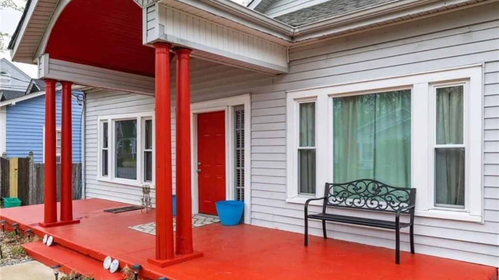 Colorful front porch with red columns, red door, and a black bench.