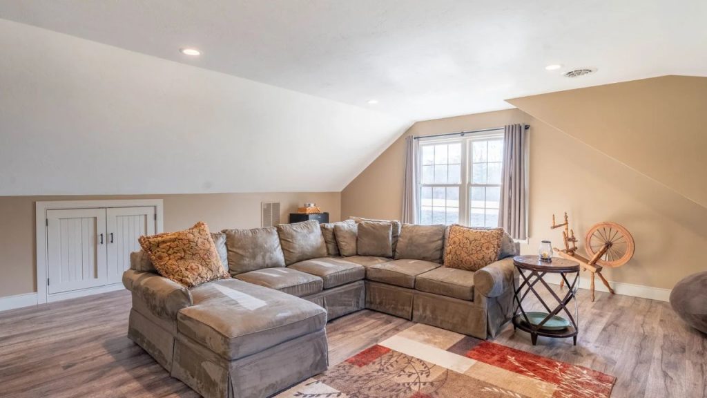 Cozy attic living room with a large sectional sofa, wood flooring, and rustic decor.