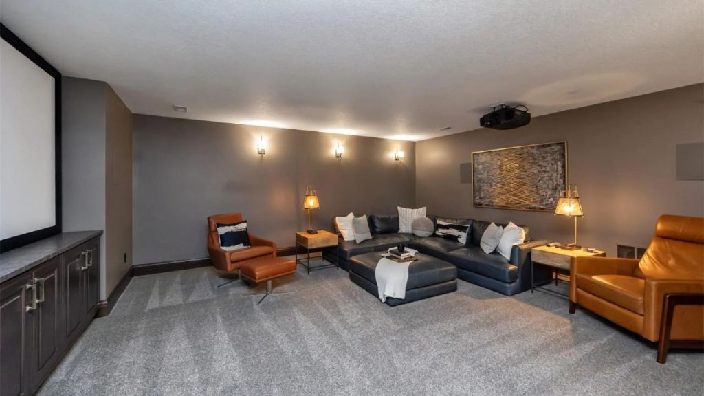 A cozy living room with a sectional sofa, projector screen, warm lighting, and built-in cabinets, creating a perfect movie night vibe.