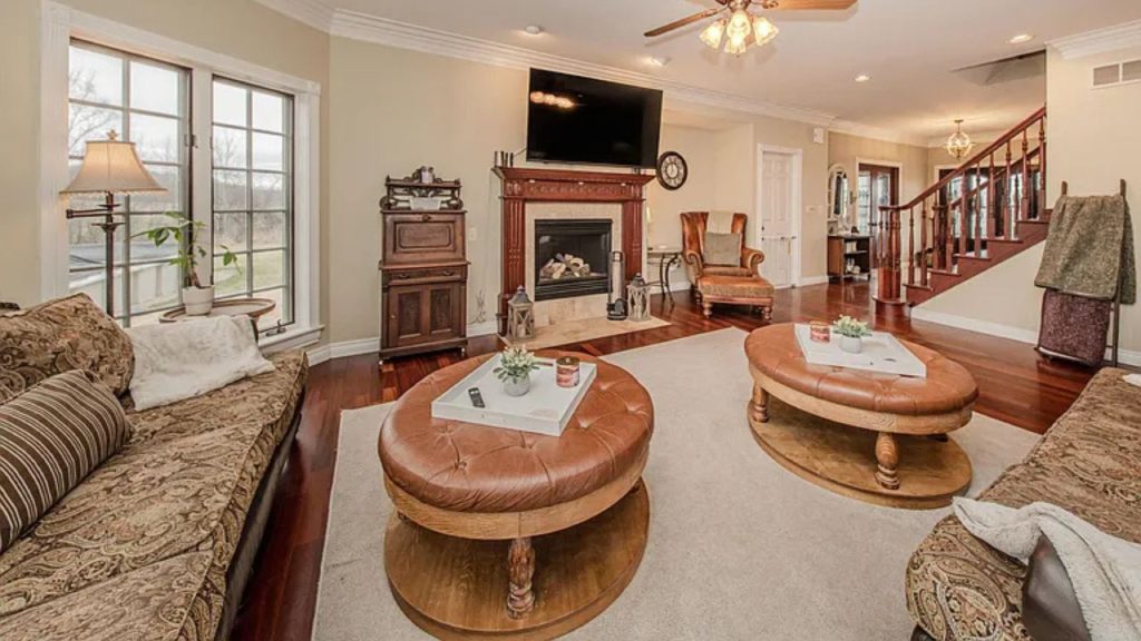 A warm living room with a fireplace, hardwood floors, large windows, and cozy furniture.