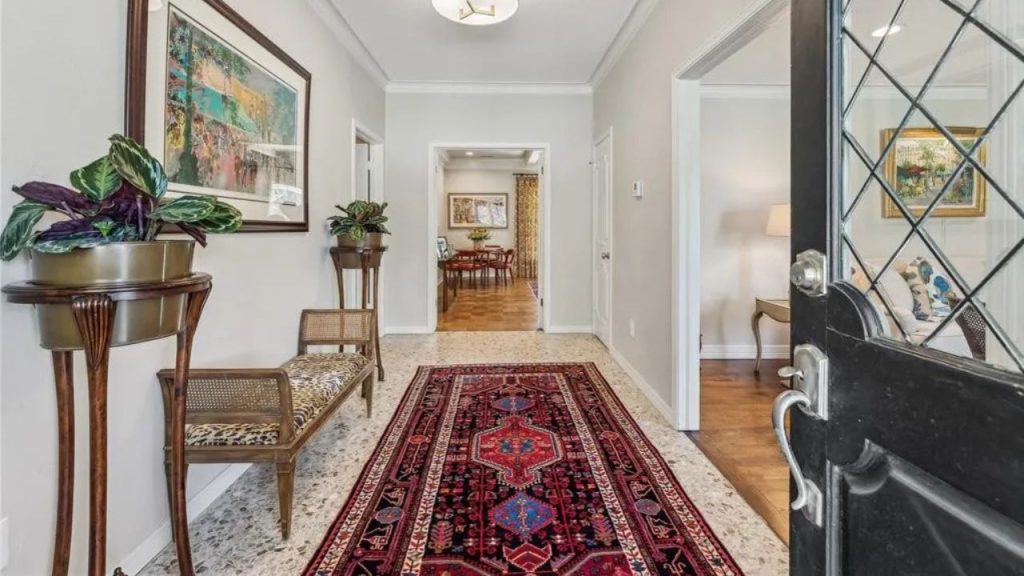 A bright foyer with a colorful rug, leopard-print bench, green plants, and artwork, leading to a dining area.