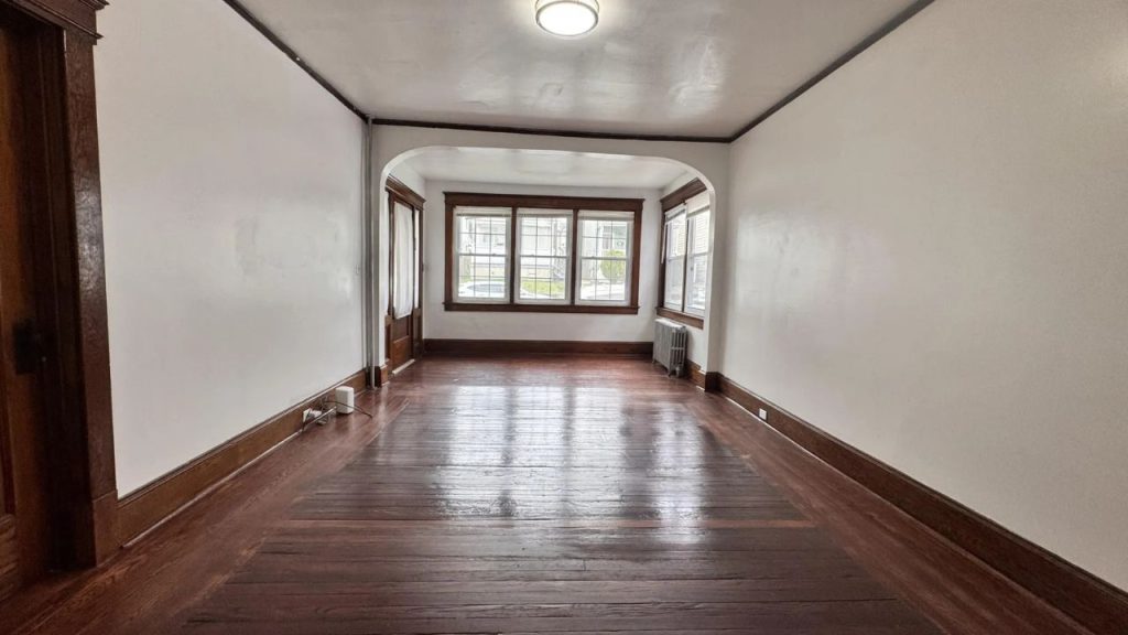 A bright hallway with hardwood floors, large windows, and an arched doorway under a ceiling light.
