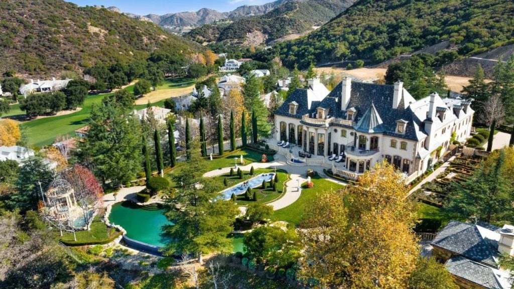 A luxurious colonial mansion with slate roofs, surrounded by lush gardens, a pool, and rolling hills.