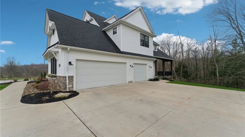 A modern home side with a double garage, white doors, and landscaped beds under a clear sky.