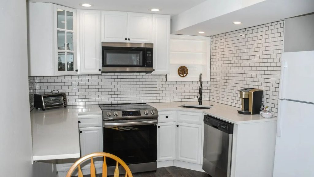 A bright kitchen with white cabinets, subway tile backsplash, and stainless steel appliances, featuring a wooden chair.