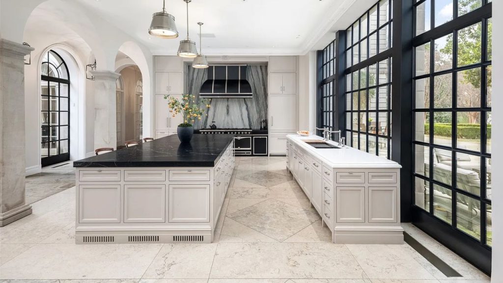 A bright kitchen with a black marble island, large windows, and elegant cabinetry.