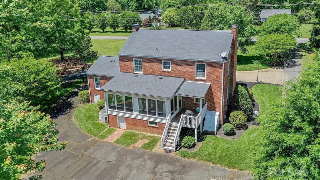 A red brick Colonial home with a bright sunroom, wooden staircase, and lush green backyard surrounded by trees.