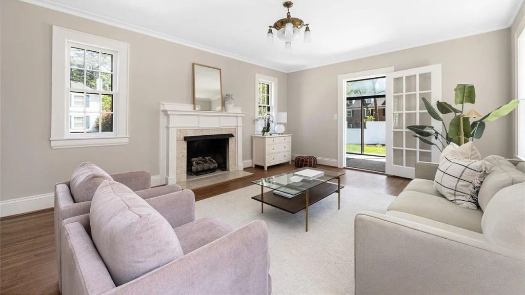 A cozy living room with a fireplace, chandelier, and open French doors to a backyard.