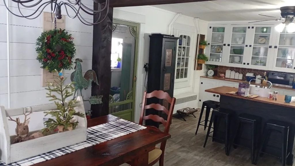 A cozy kitchen nook with a wooden table, festive decor, glass cabinets, and black barstools at an island.