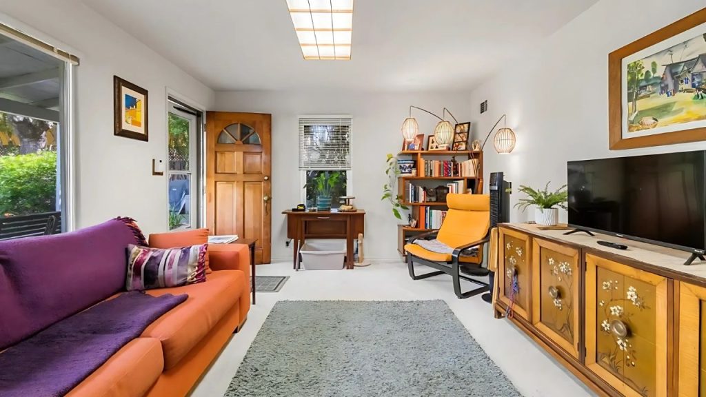A cozy living room with orange furniture, purple sofa, bookshelf, and floral TV unit.