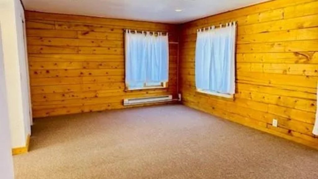 Room with pine walls, carpet floor, and white curtains.