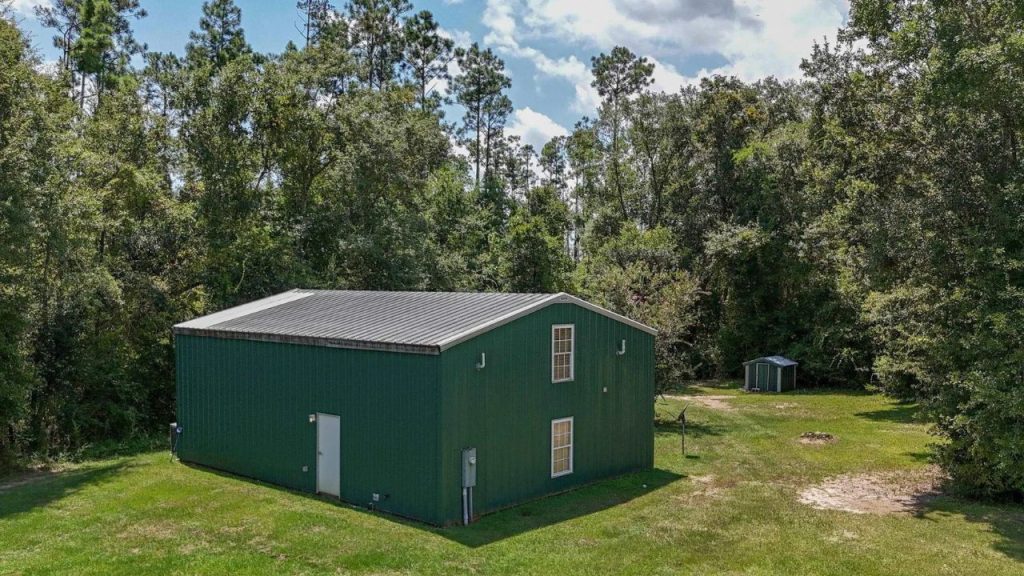 Green metal cabin surrounded by tall trees and grass.