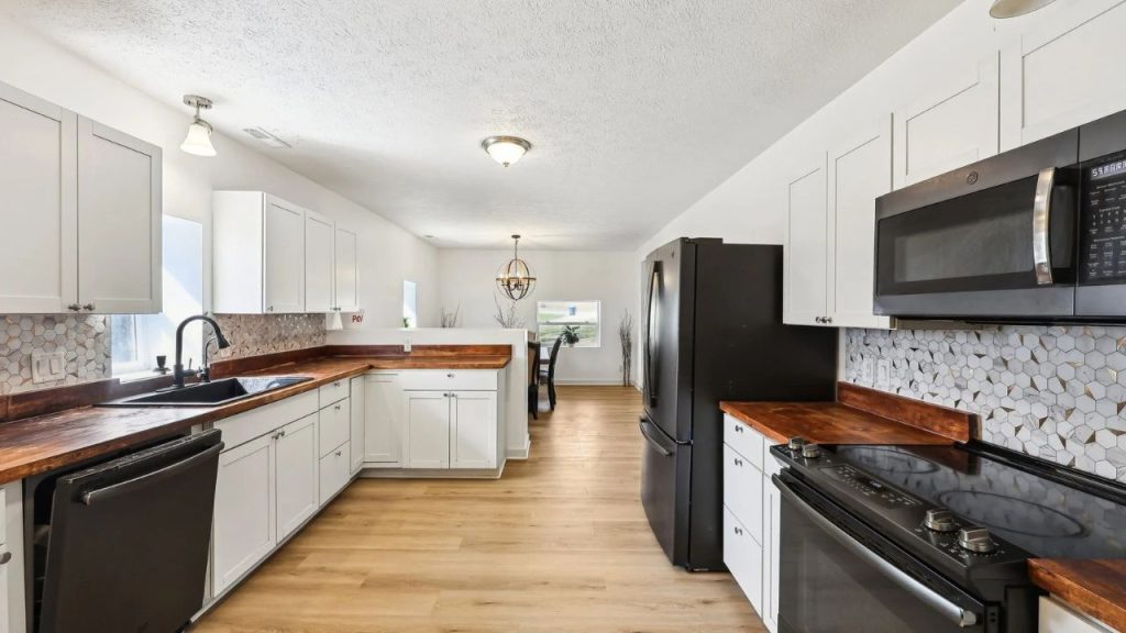 Kitchen with white cabinets, wood countertops, and black appliances.